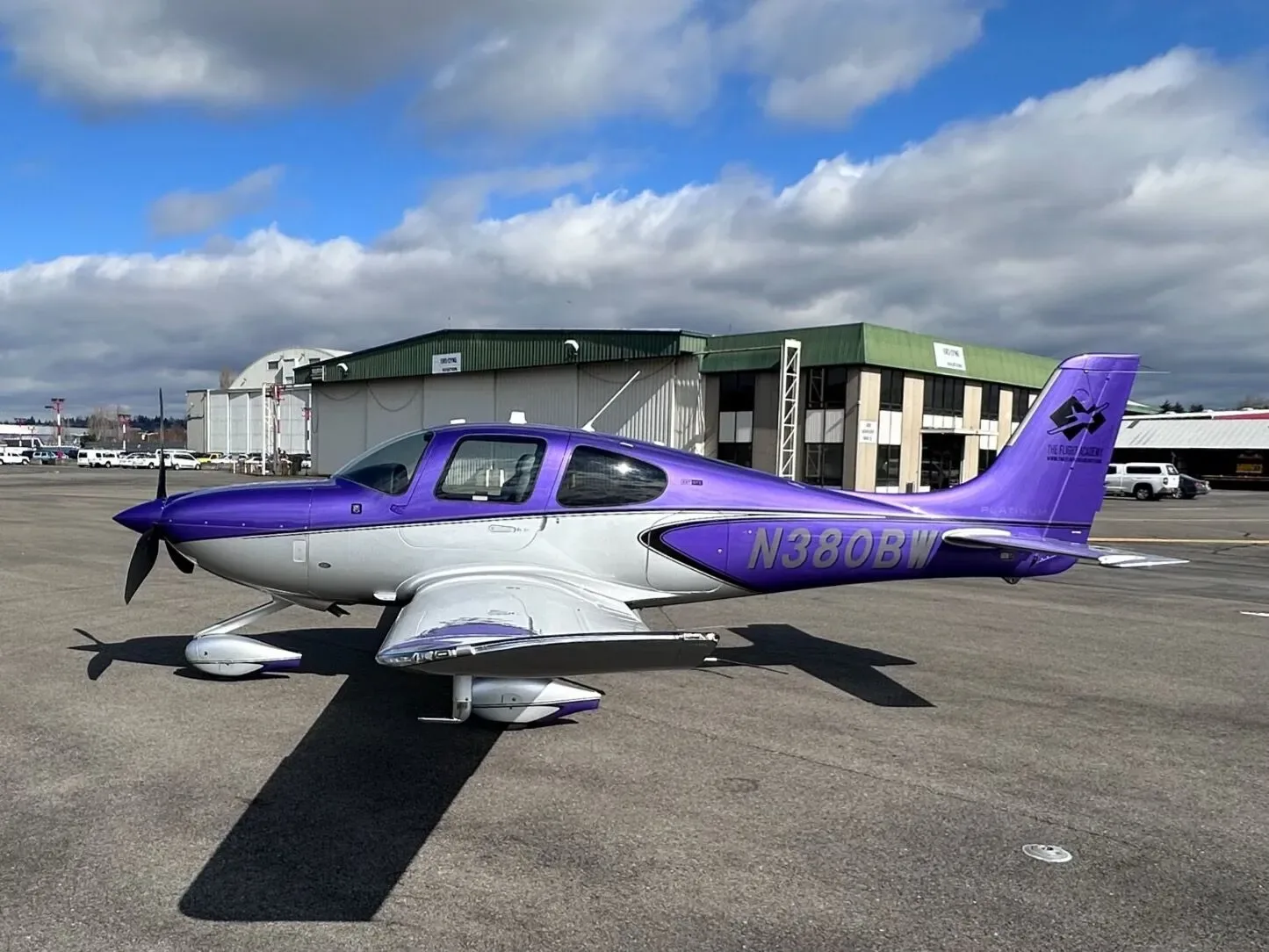 A purple and silver Cirrus SR22 aircraft, N380BW, parked on an airport tarmac under a partly cloudy sky.
