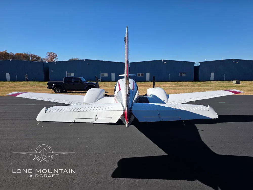 A rear view of the white and red twin-engine aircraft, N1HB, parked on an airfield.
