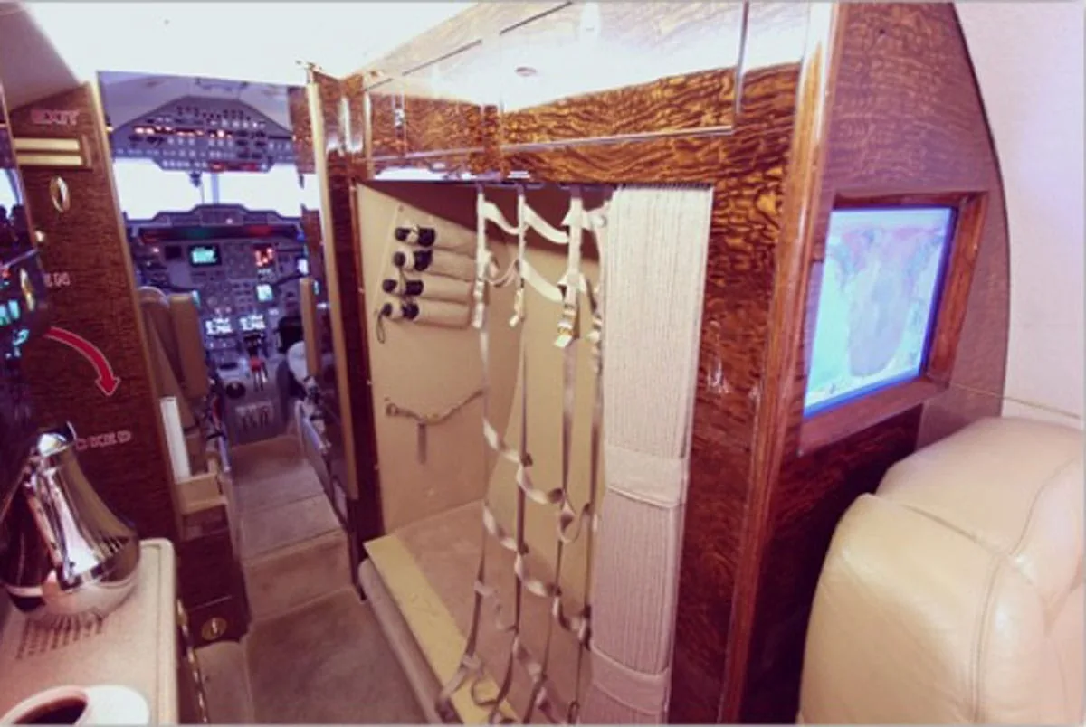 View from the aircraft cabin looking forward into the galley and towards the cockpit, featuring wood paneling and a small screen.
