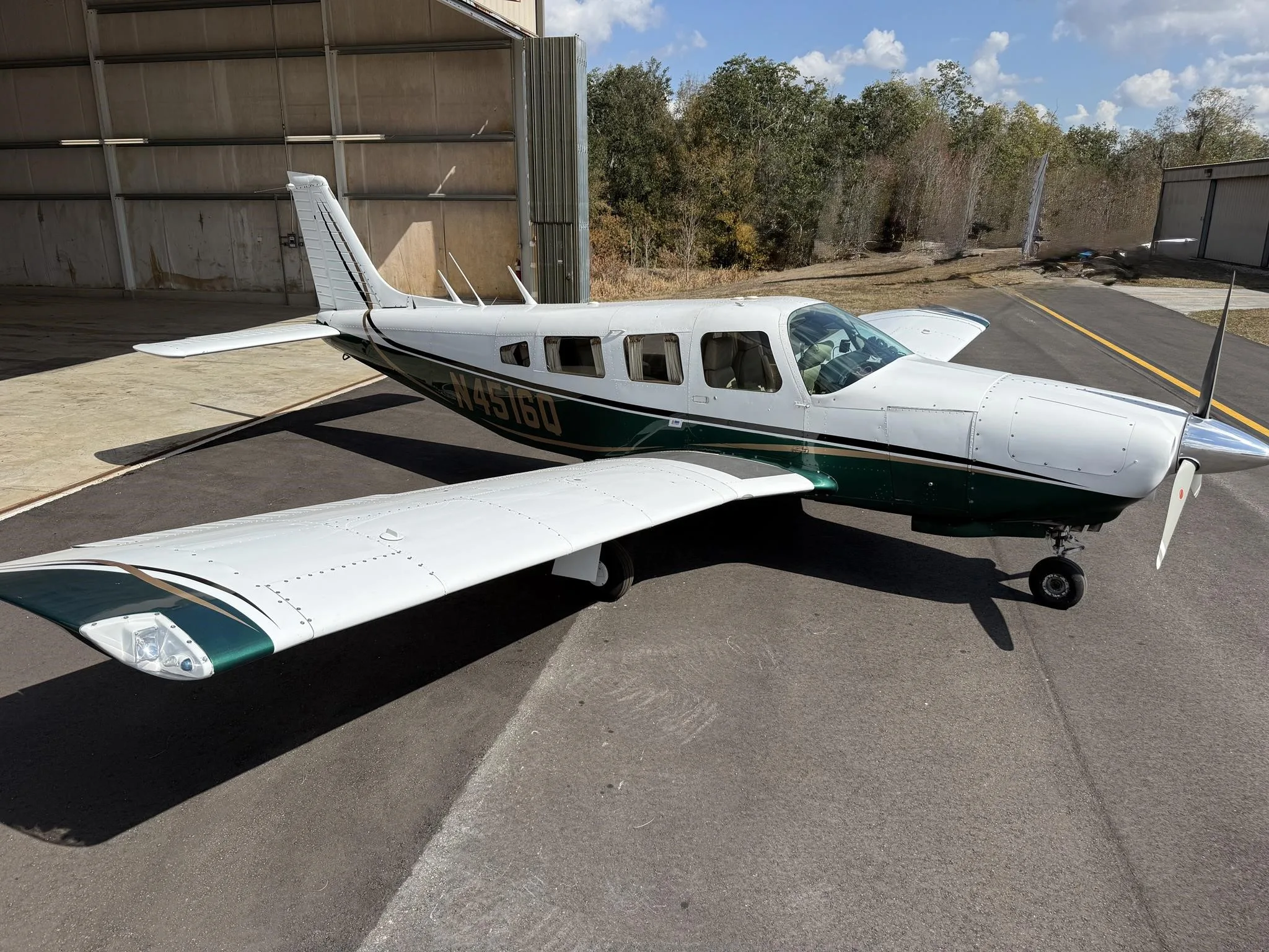 A white and green Piper PA-32R-300 Cherokee Lance II (N4516Q) parked on an asphalt ramp outside a hangar.
