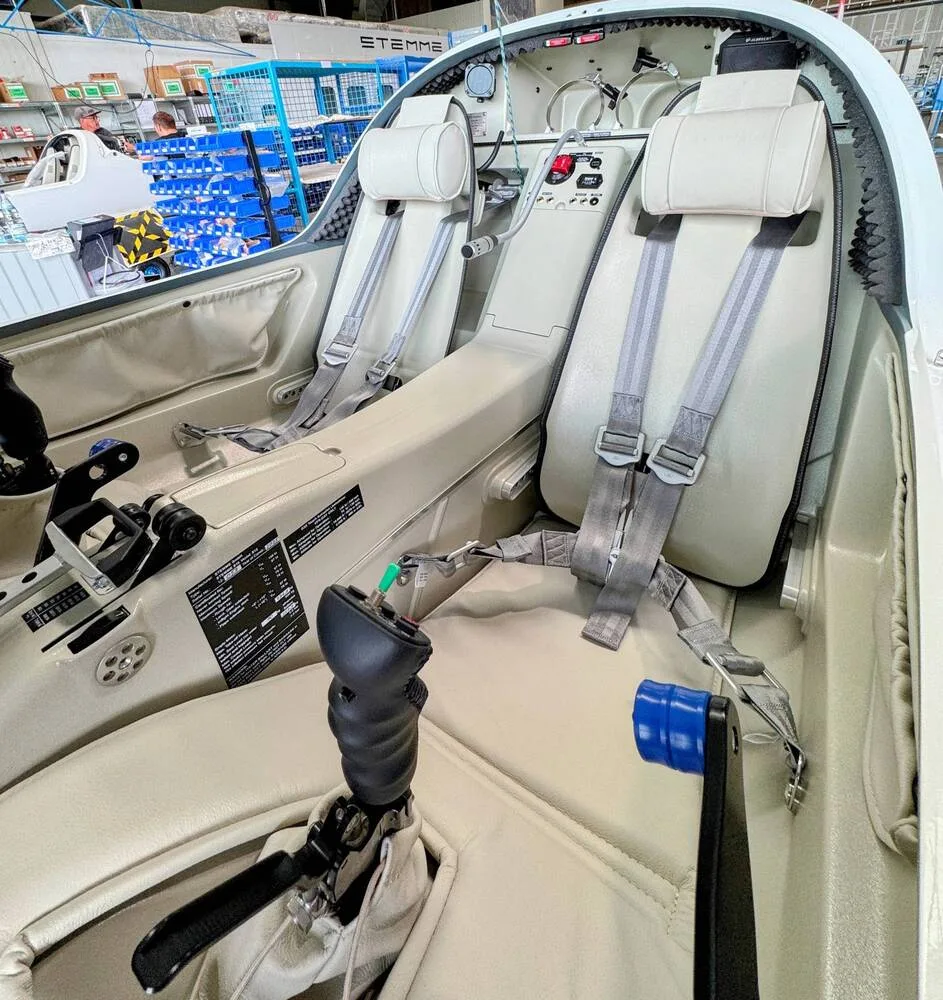 The beige interior cabin of a Stemme S12 motorglider, showing two seats with harnesses and flight controls.