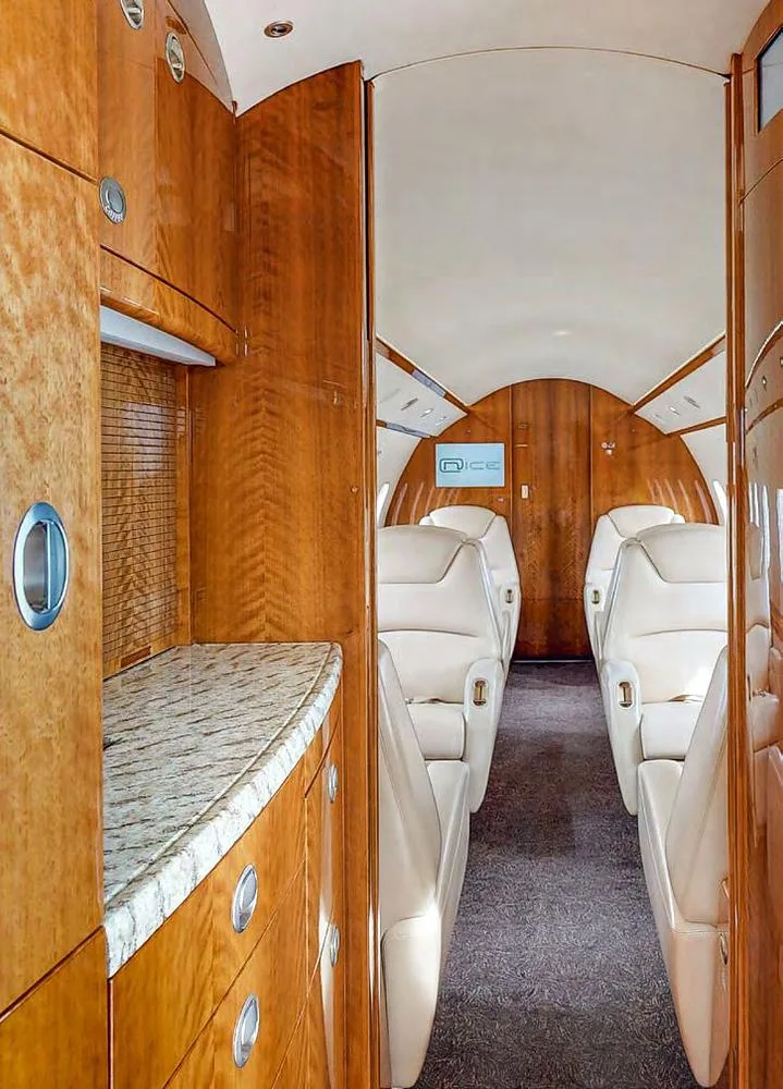 The aircraft cabin interior showing a galley area with wood cabinetry and a granite countertop, looking towards the passenger seating.