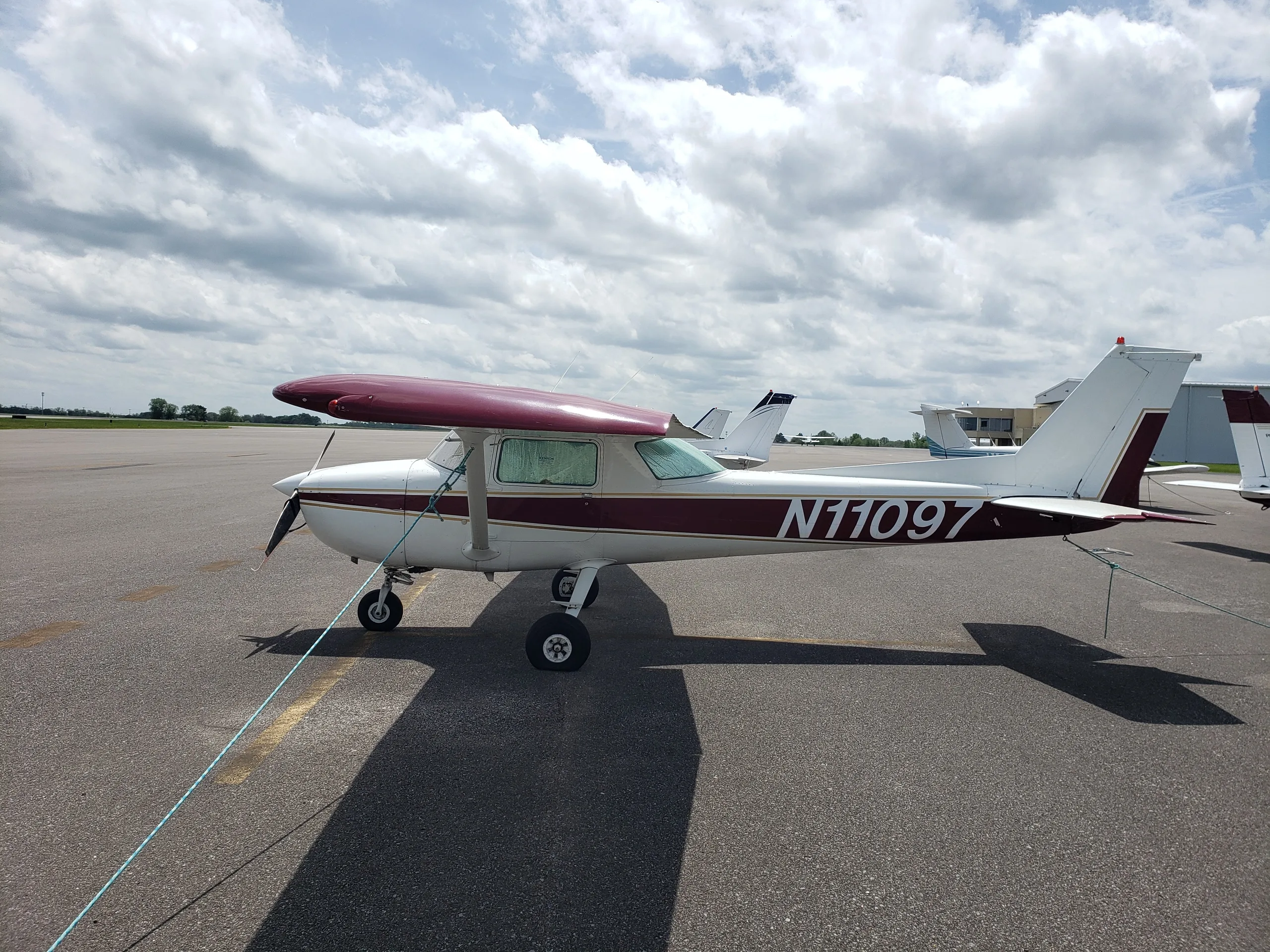 A white and maroon Cessna 150 or 152 aircraft, N11097, parked on an asphalt ramp under a cloudy sky.