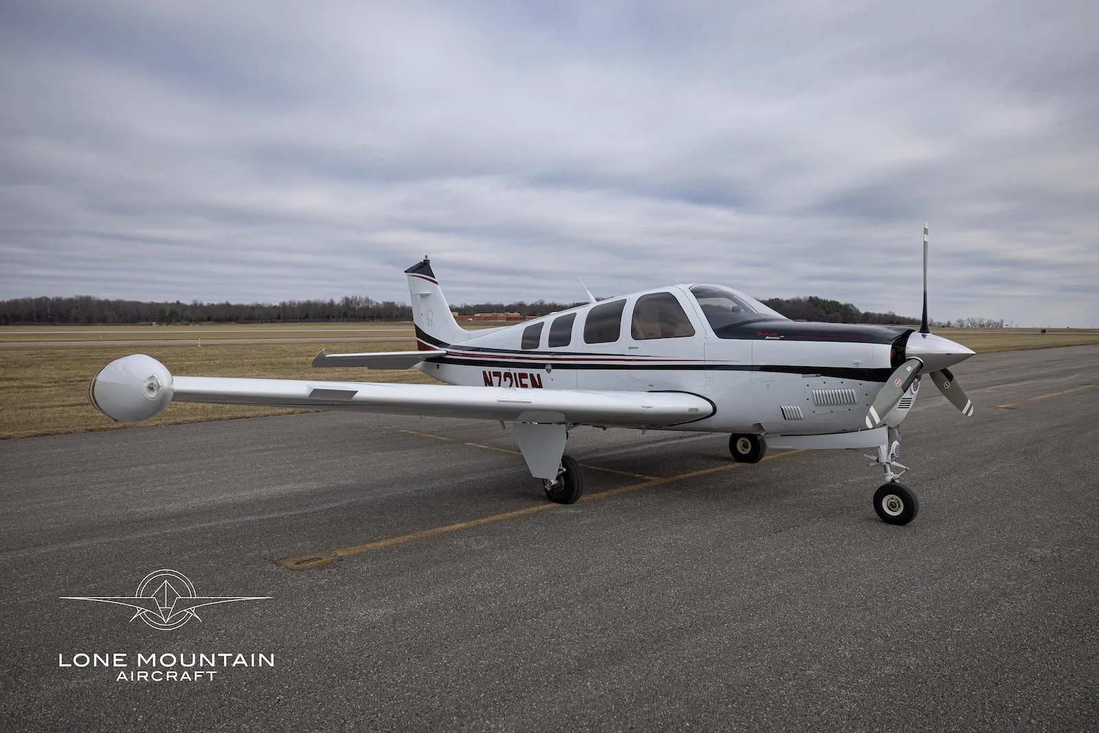 A three-quarter front view of the N721EN single-engine propeller aircraft, showing its white, black, and red paint scheme on an airfield.