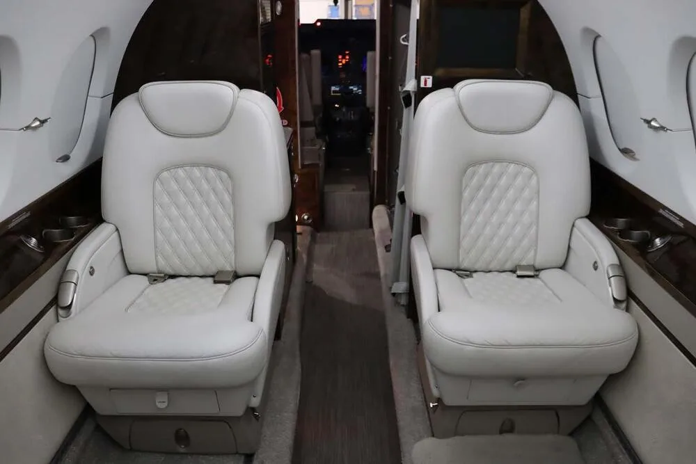 A view of the aircraft's cabin interior with light grey quilted leather seats, looking forward towards the cockpit.