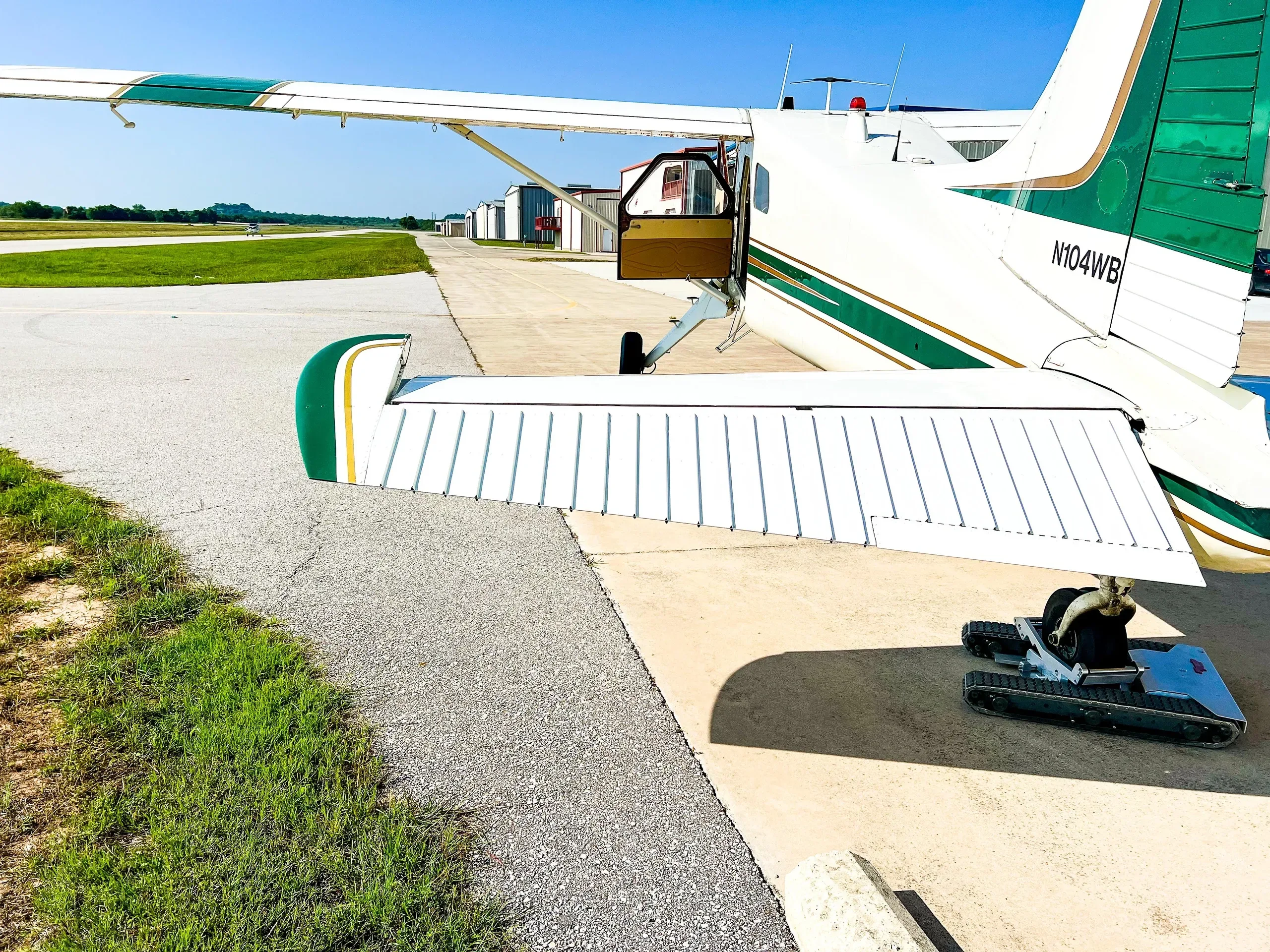 Rear quarter view of the N104WB aircraft on an airfield, showing its tail, wing, and open door.