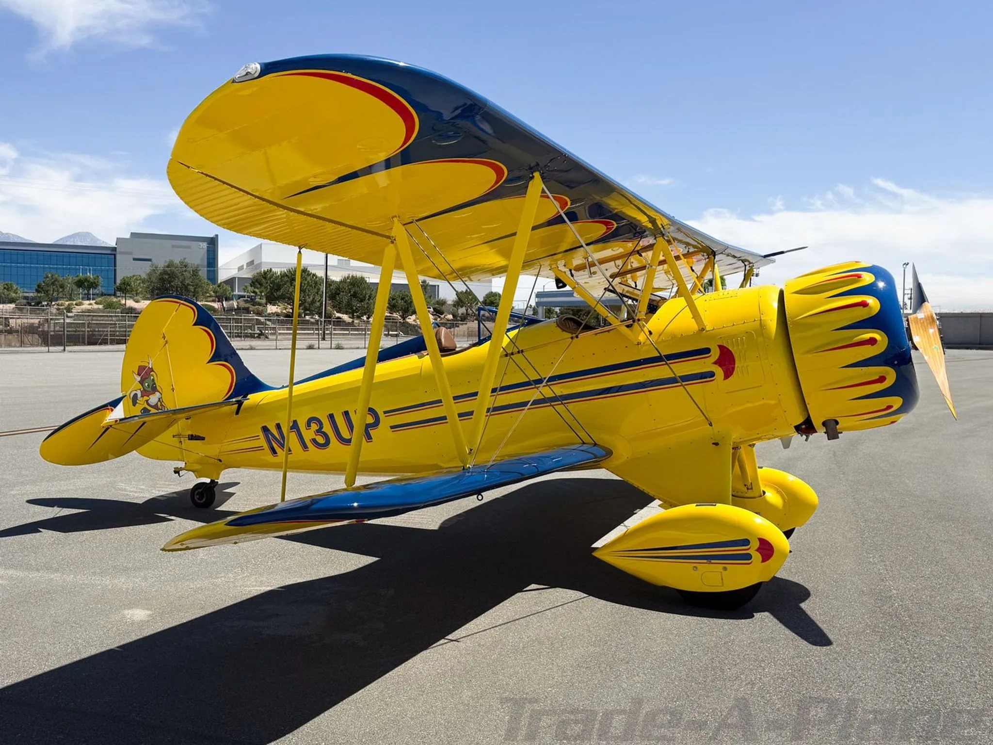 A three-quarter front view of a yellow and blue biplane with registration N13UP on an airfield.