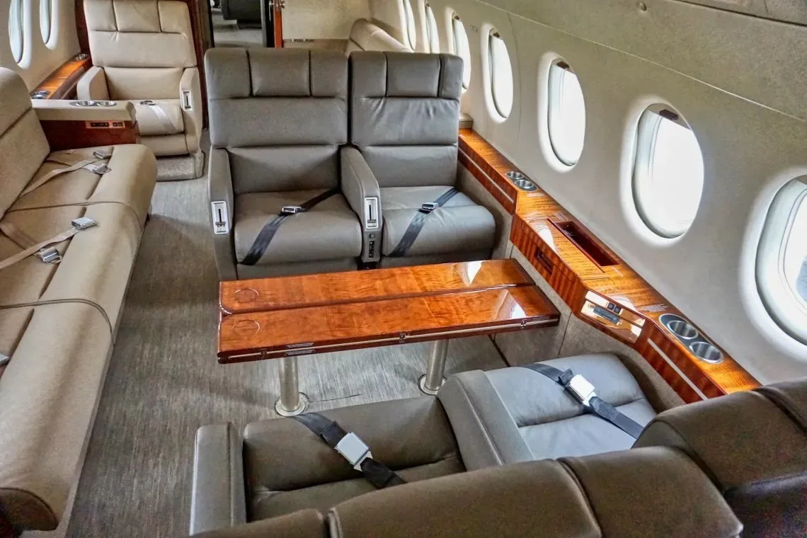 The aircraft's interior features leather seats, wood trim, and a table.