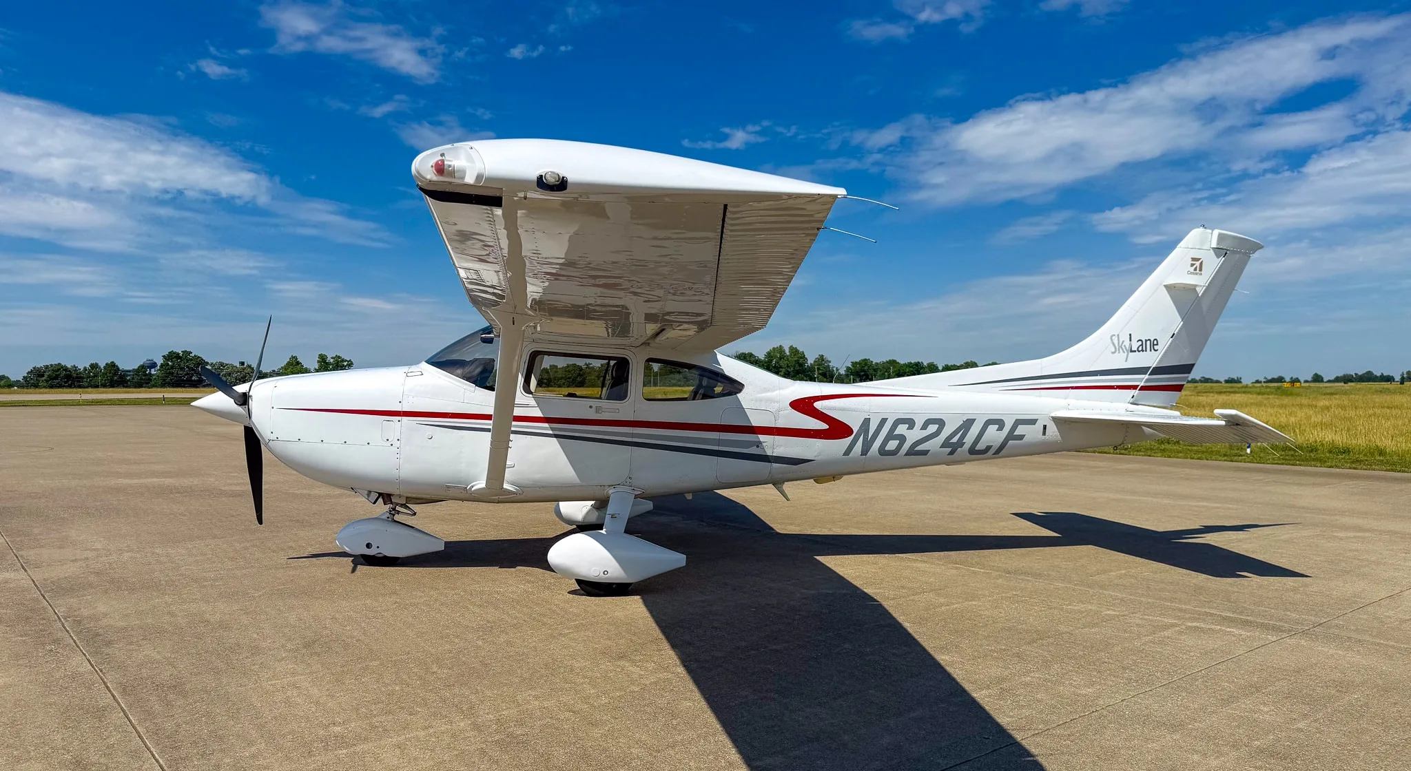 Side view of a white Cessna 182 Skylane with red and gray stripes, registration N624CF, parked on an asphalt ramp.