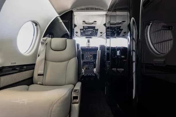 View from the aircraft cabin looking forward towards the cockpit, showing light grey seats and dark cabinetry.