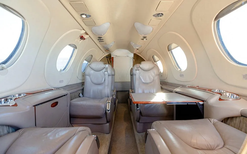 The beige interior cabin of a private jet, featuring comfortable seating and a small table.