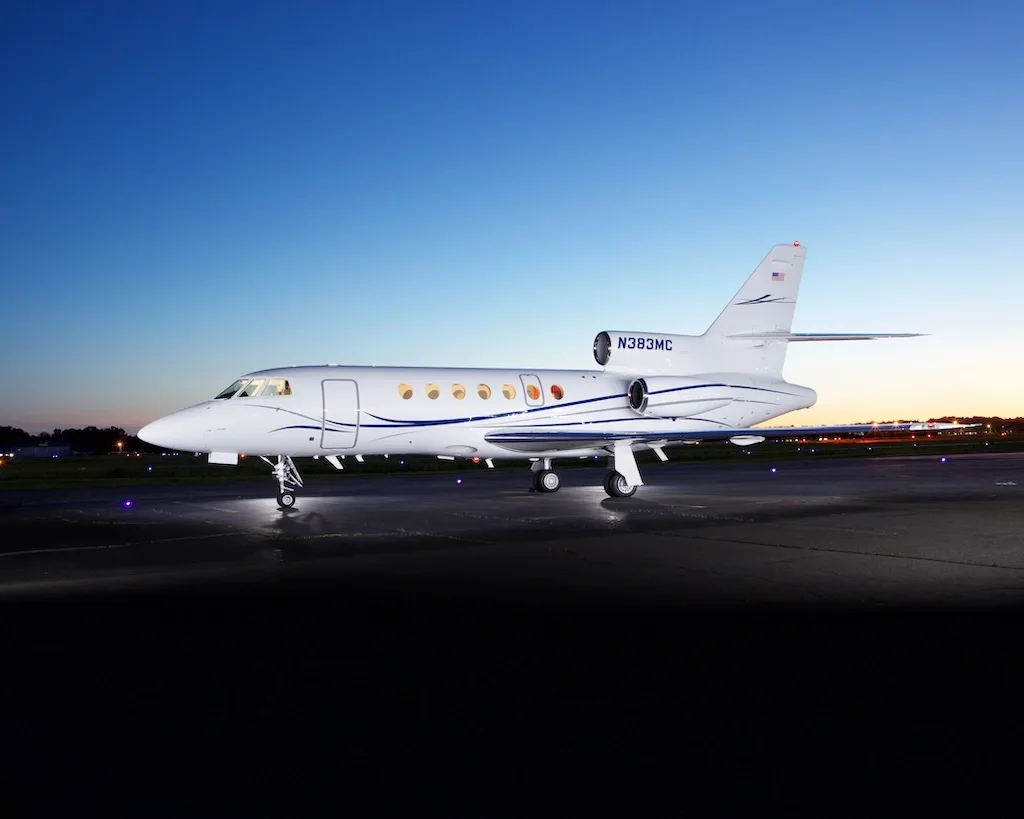 A white business jet, N383MC, with blue and grey stripes, parked on a tarmac at dusk.