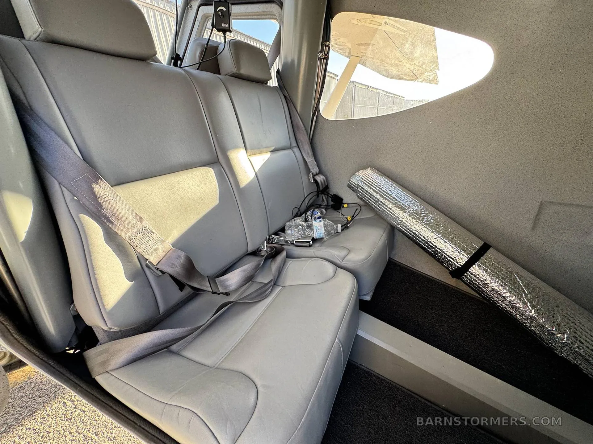 The light gray rear seats of a small aircraft cabin, with a rolled-up reflective mat on the floor.
