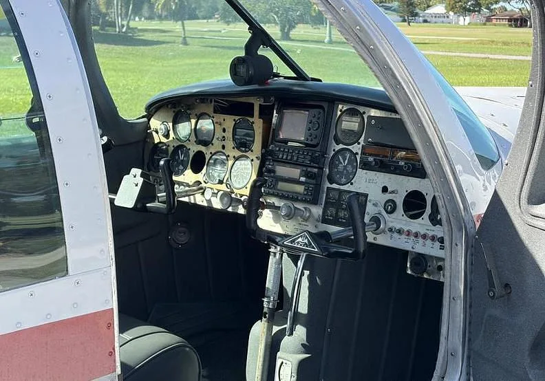 The cockpit of a small aircraft, showing the instrument panel and controls from the side.