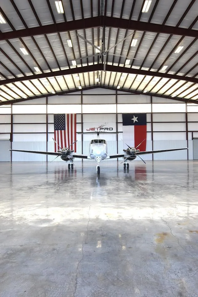 A low-angle, head-on view of the white and blue Beechcraft King Air twin-engine turboprop aircraft, N627MG, in a hangar.