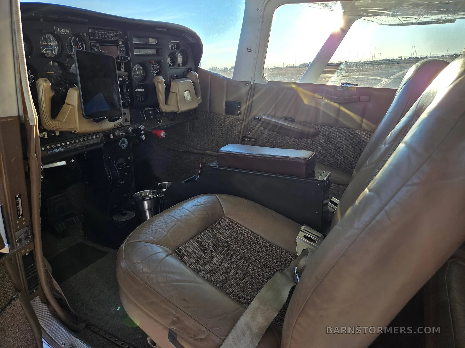 The cockpit interior of a Cessna aircraft, showing the instrument panel, controls, and brown leather seats.