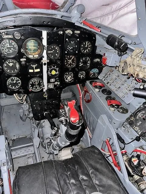 The cockpit of a vintage jet aircraft, showing the instrument panel, control stick, and side console.