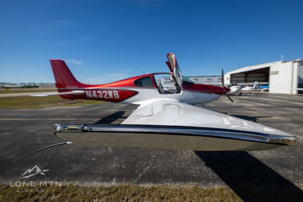 A close-up view of the wingtip and front fuselage of the red and white Cirrus SR20 aircraft (N432WB) with its doors open.