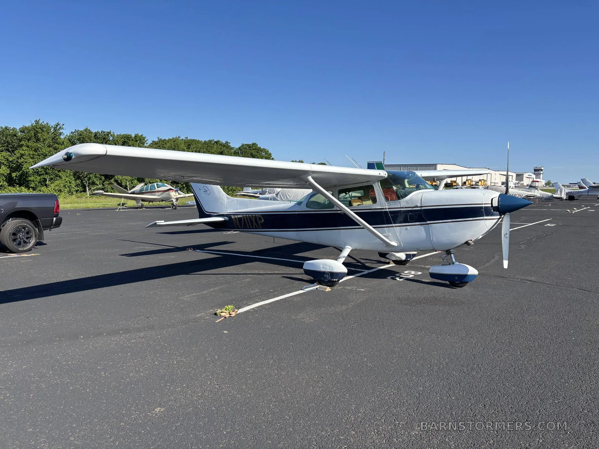 A white and blue Cessna 172 (N77XP) parked on an asphalt ramp on a sunny day.