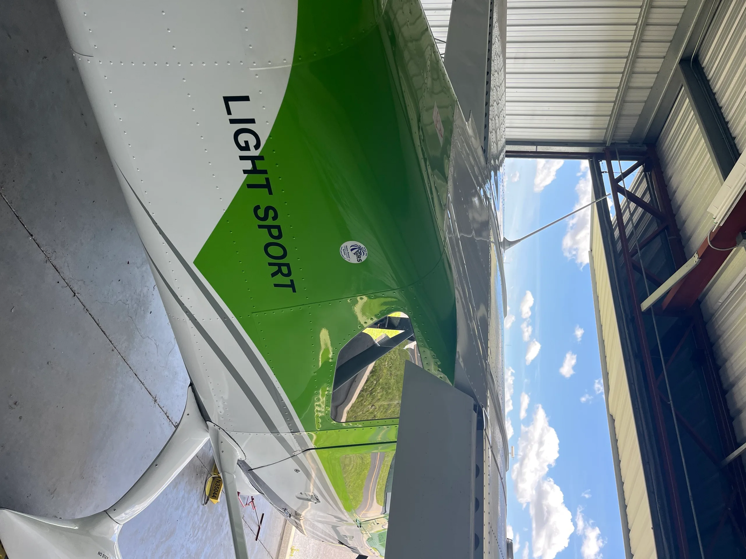 A close-up side view of the green and white fuselage of a Colt light sport aircraft, showing the wing and 'LIGHT SPORT' text.