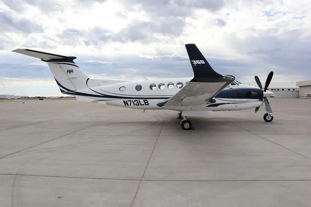 A side view of the white and dark blue Beechcraft King Air 360, registration N713LB, parked on an airport tarmac.