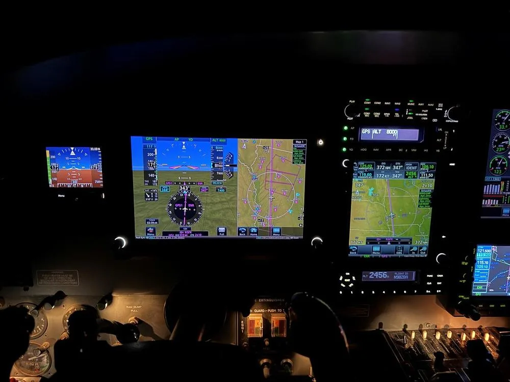 A dark cockpit view showing multiple illuminated digital display screens and analog gauges.