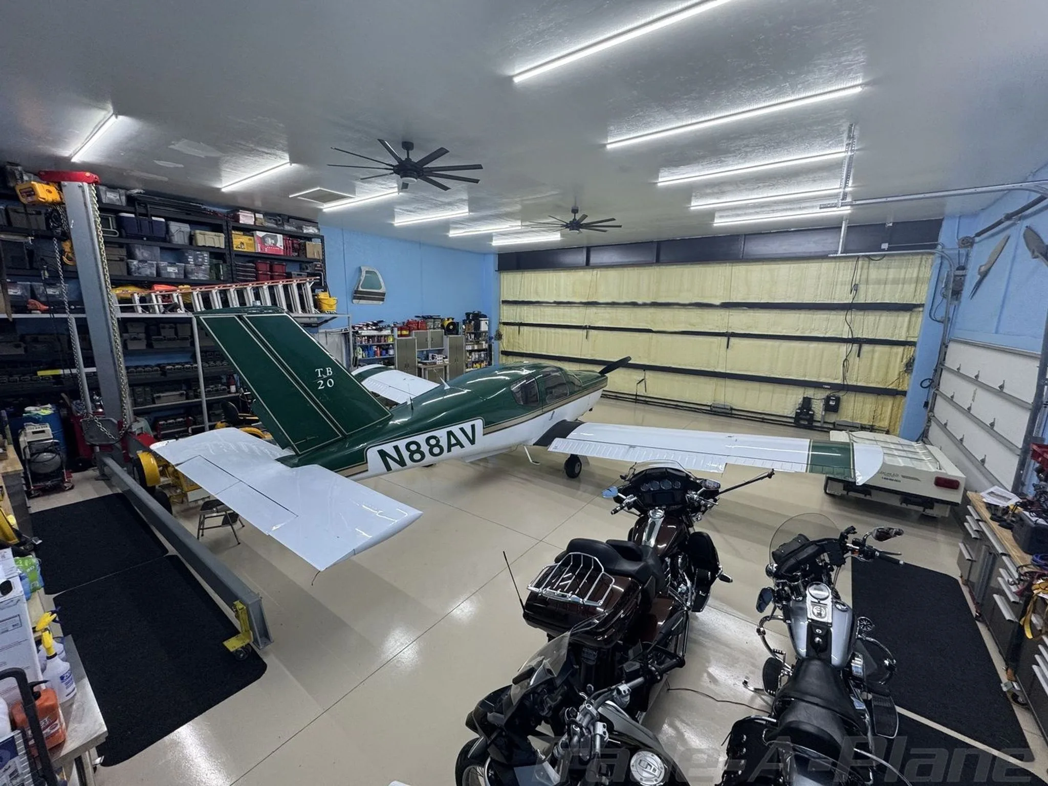 An overhead view of a green and white single-engine aircraft (N88AV) parked inside a hangar with motorcycles.