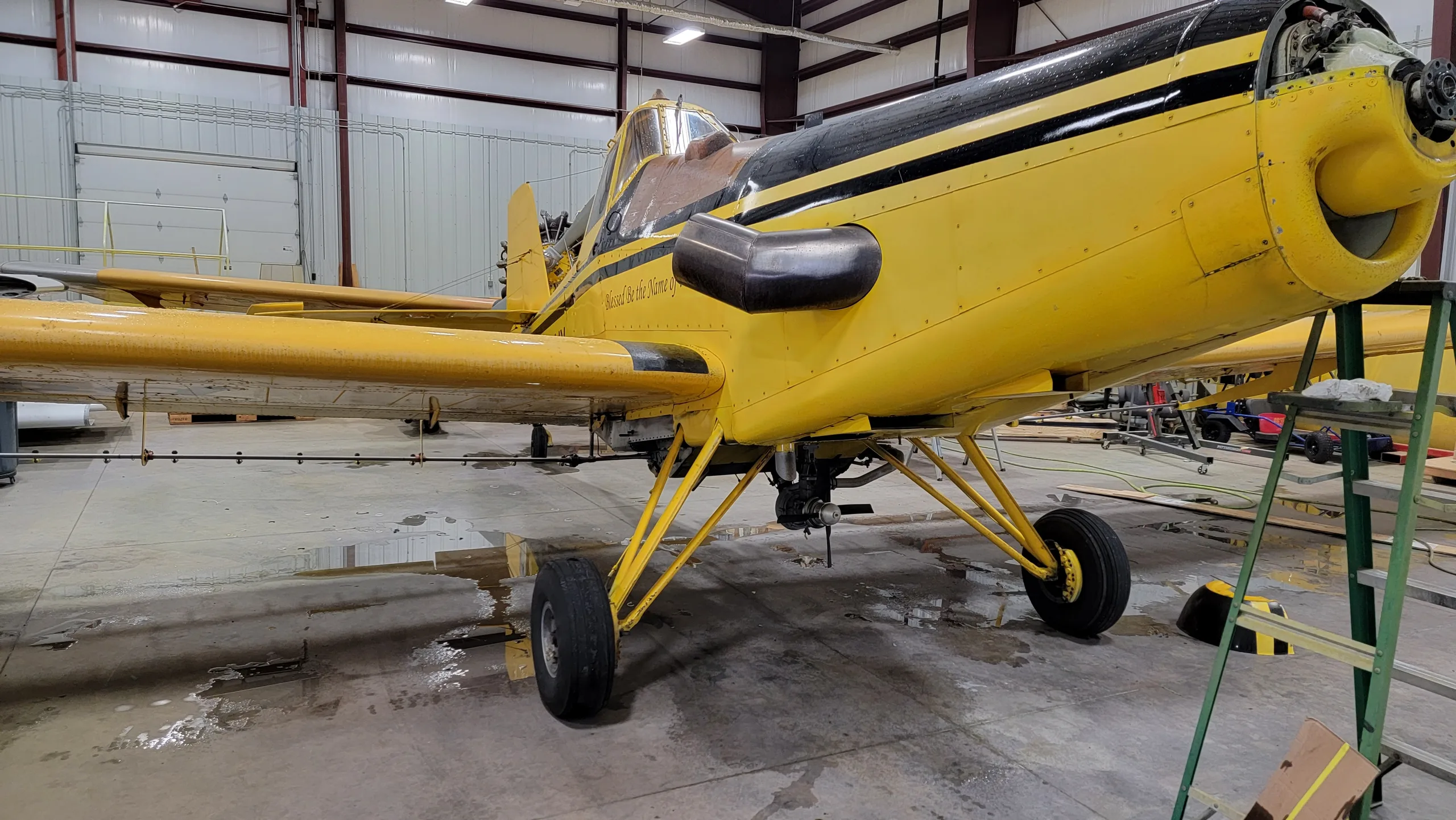 A front-side view of the yellow and black crop duster aircraft, N4941X, with its engine cowling partially removed, inside a hangar.