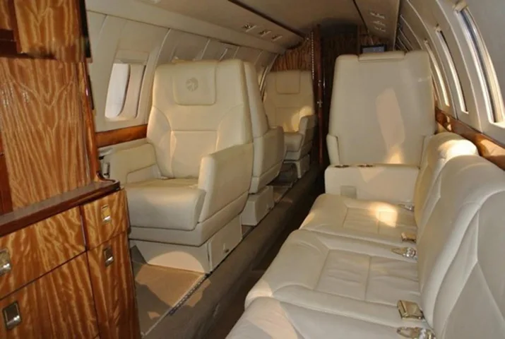 The luxurious interior cabin of a private jet with light cream leather seats and polished wood cabinetry.