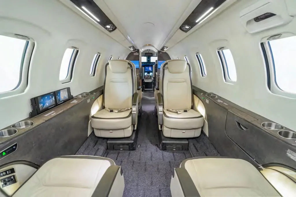 A wider view of the business jet's interior cabin, showing multiple light beige leather seats and side consoles.
