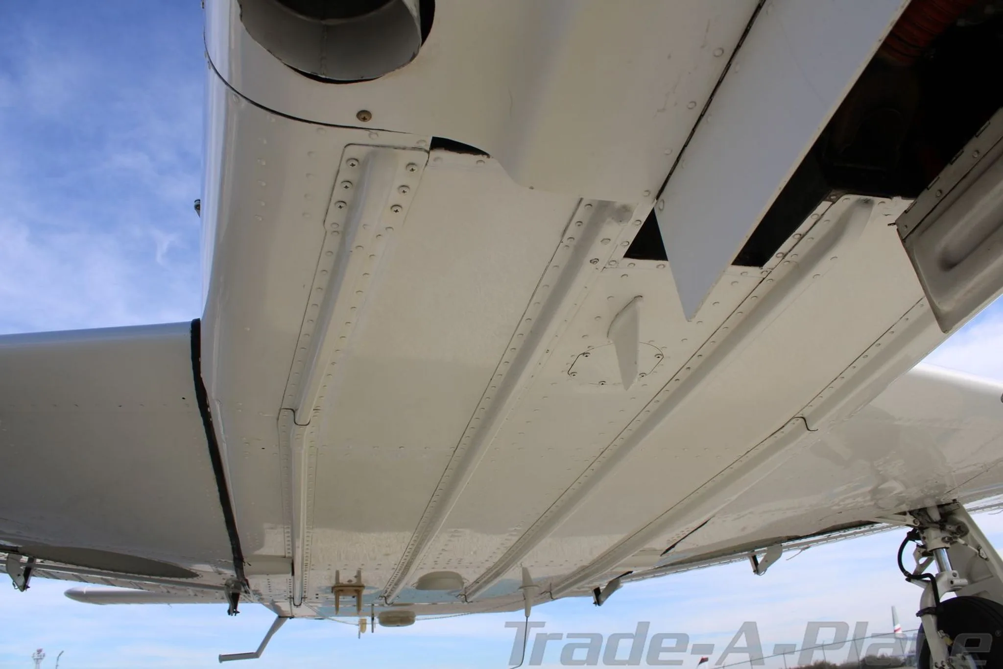 An underside view of the white Piper aircraft, showing the belly and landing gear components.