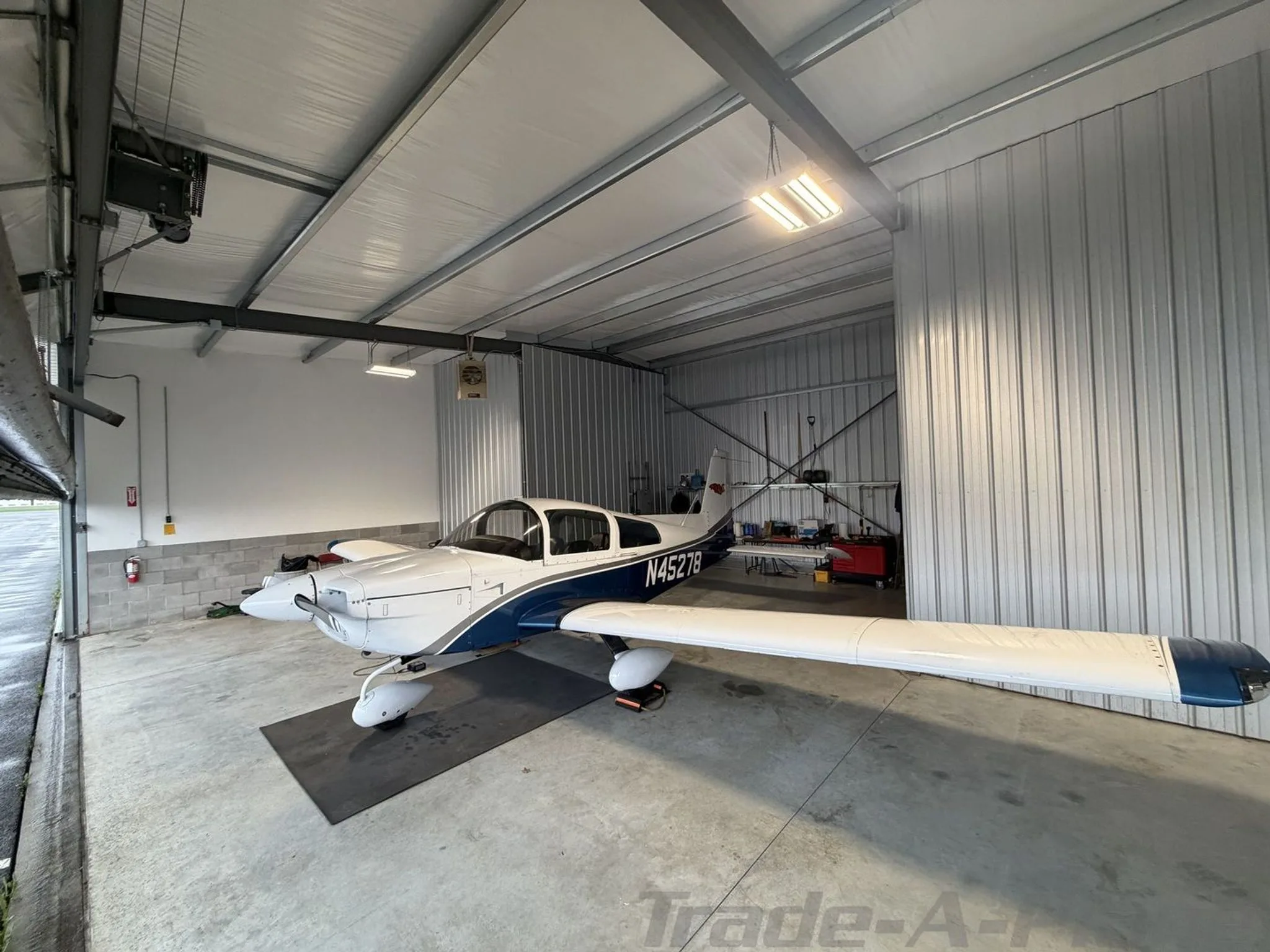 Front-left view of a white and blue Grumman AA-5B Tiger N45278 parked on a mat in a hangar.