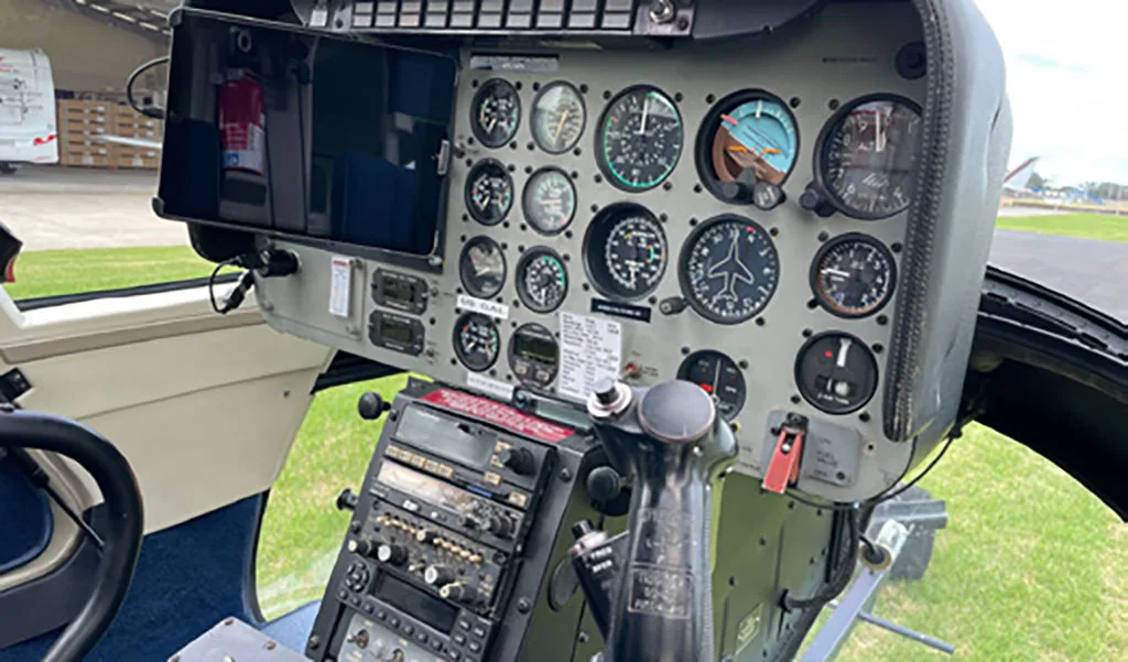 The helicopter cockpit showing the instrument panel with multiple gauges and a control stick.