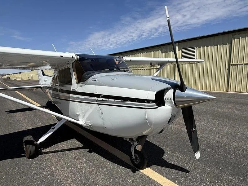 A close-up front-right view of the propeller and nose of the white Cessna 172, N738YW, on a tarmac.