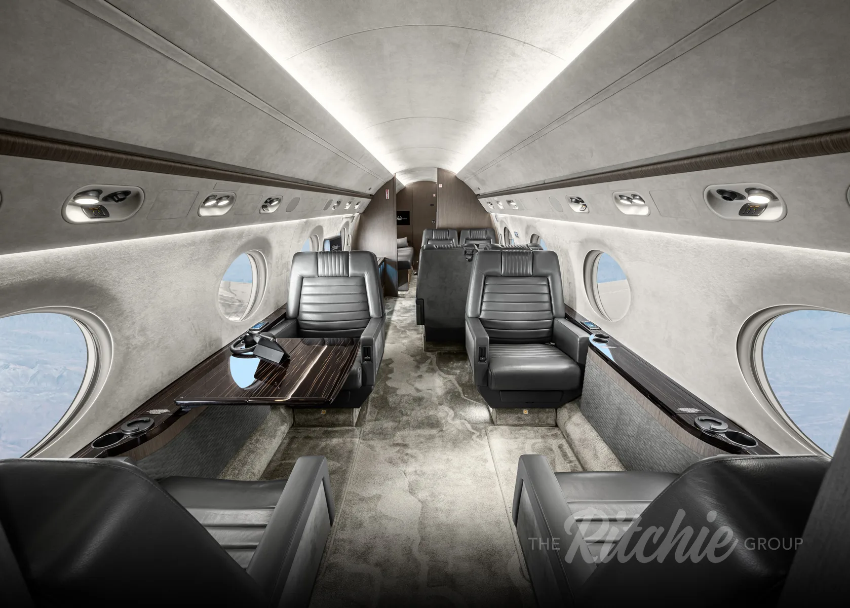 The luxurious cabin interior of a Gulfstream G650, featuring grey leather seats and a dark wood table.