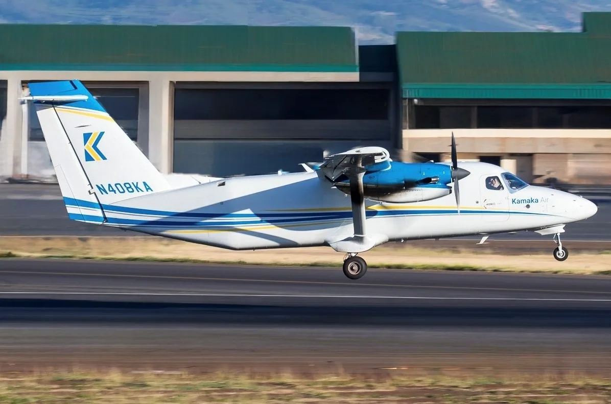 A white and blue twin-engine turboprop aircraft, N408KA, is seen in motion on a runway with a building in the background.