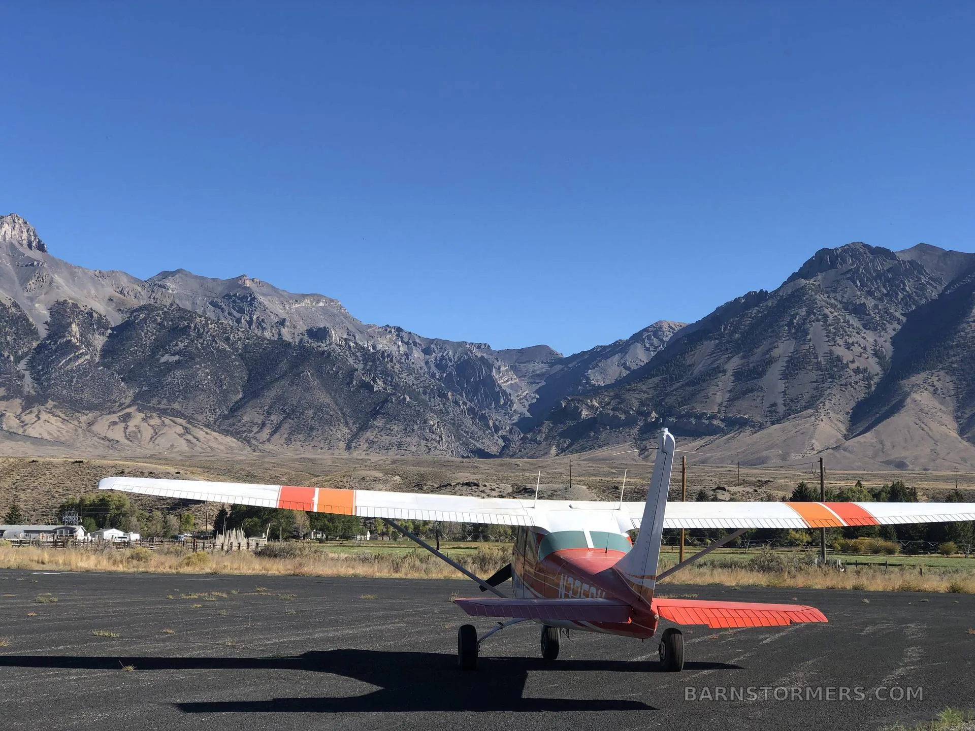 A red and white Cessna 182 Skylane is parked on an asphalt runway with mountains in the background.