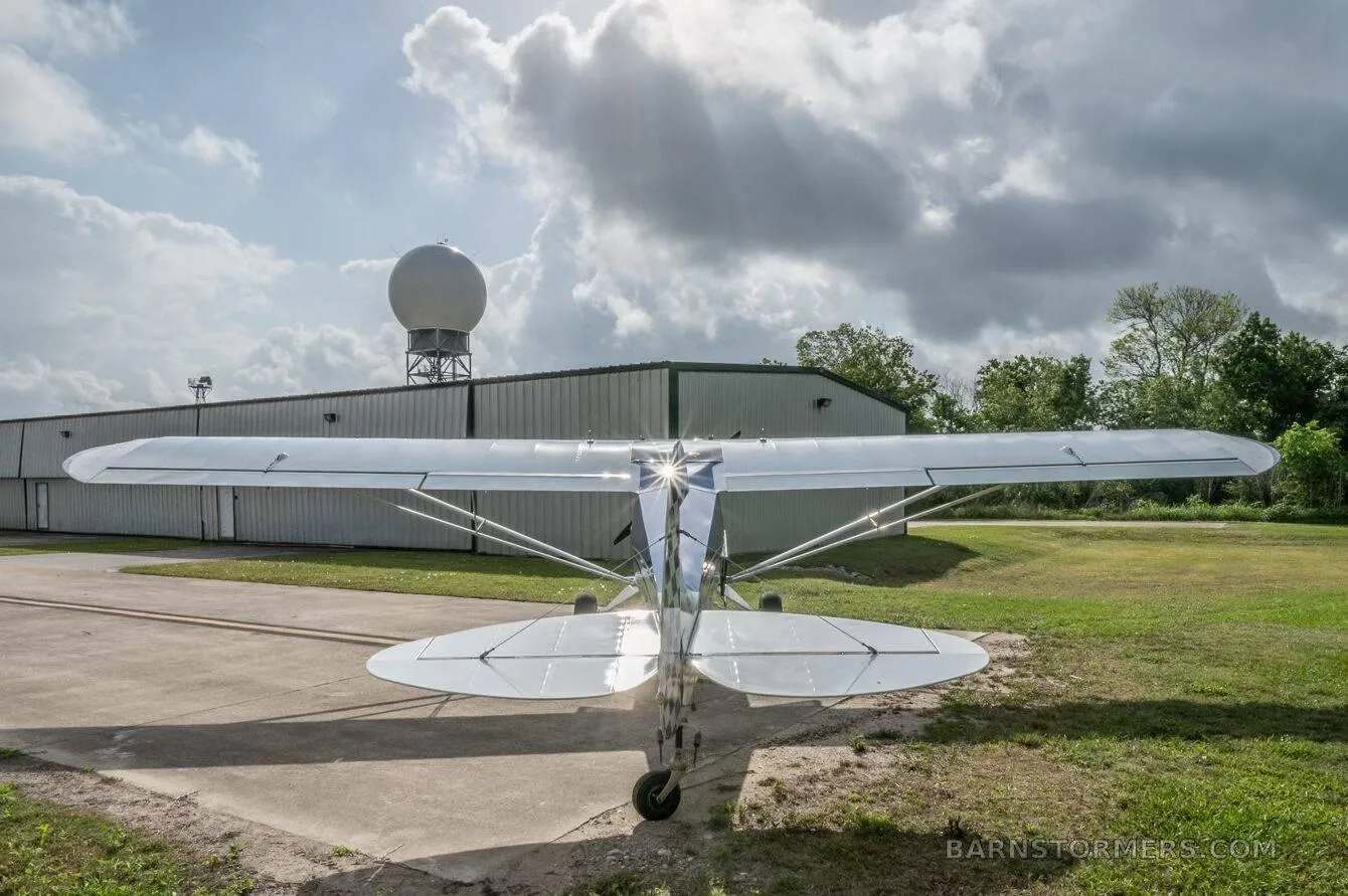 A blue and white single-engine taildragger aircraft (N6990R) is viewed from the rear, parked in front of a hangar.