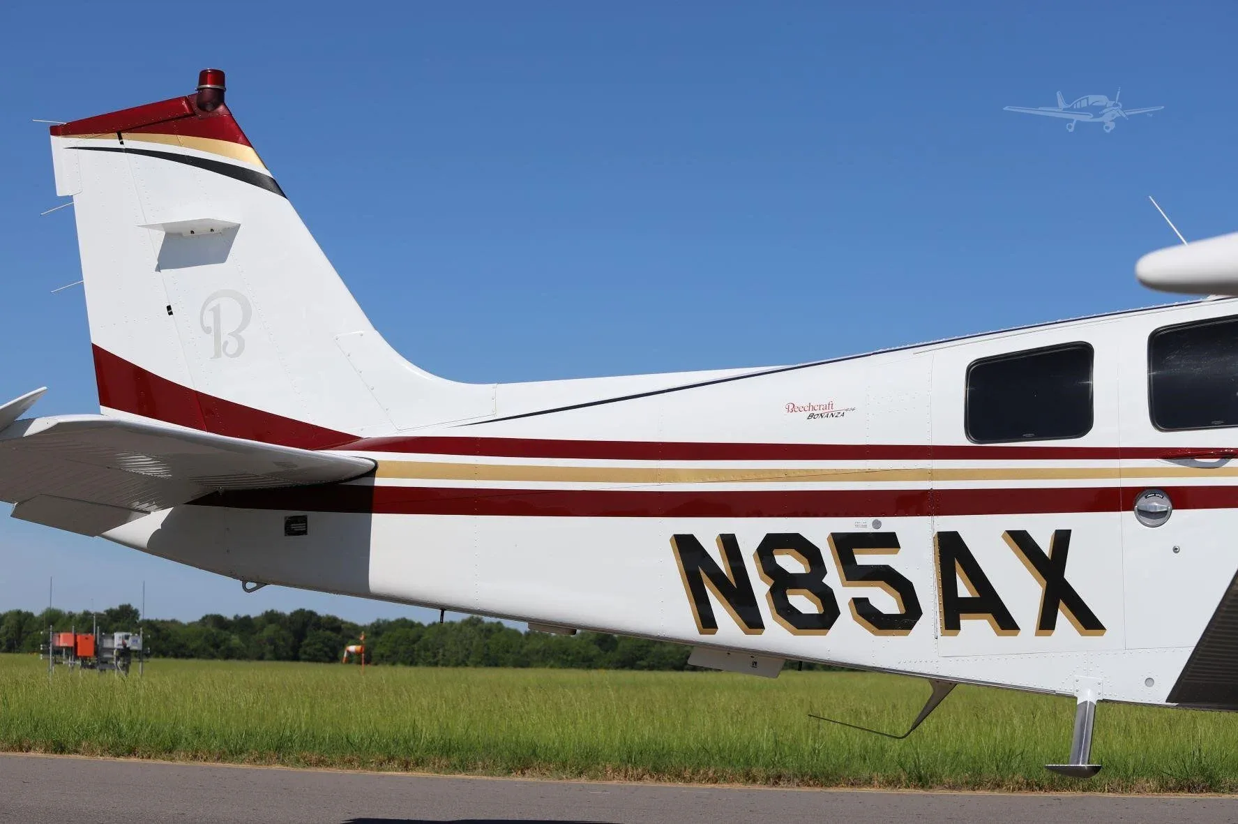 A close-up view of the tail section of a white aircraft with red and gold stripes, showing the registration N85AX.