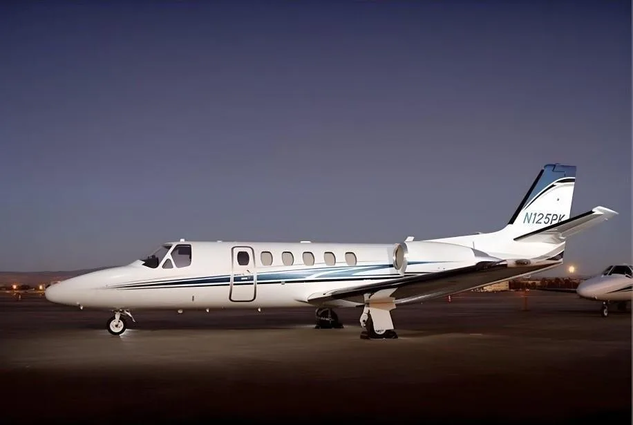 A white business jet with blue and black stripes on the fuselage and tail, parked on a tarmac at dusk.