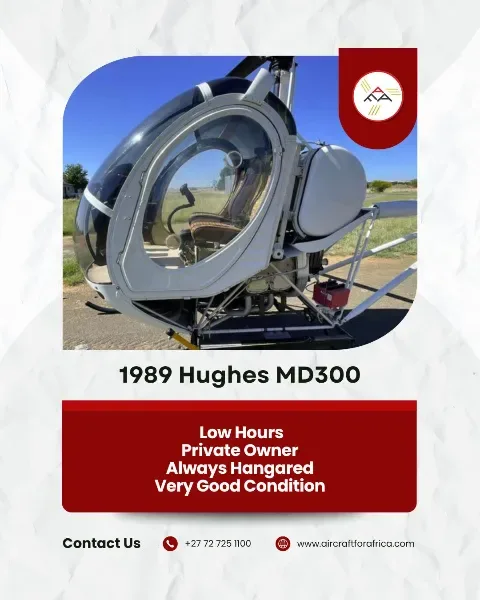 A white 1989 Hughes MD300 helicopter with a clear bubble canopy, parked on the ground under a blue sky.