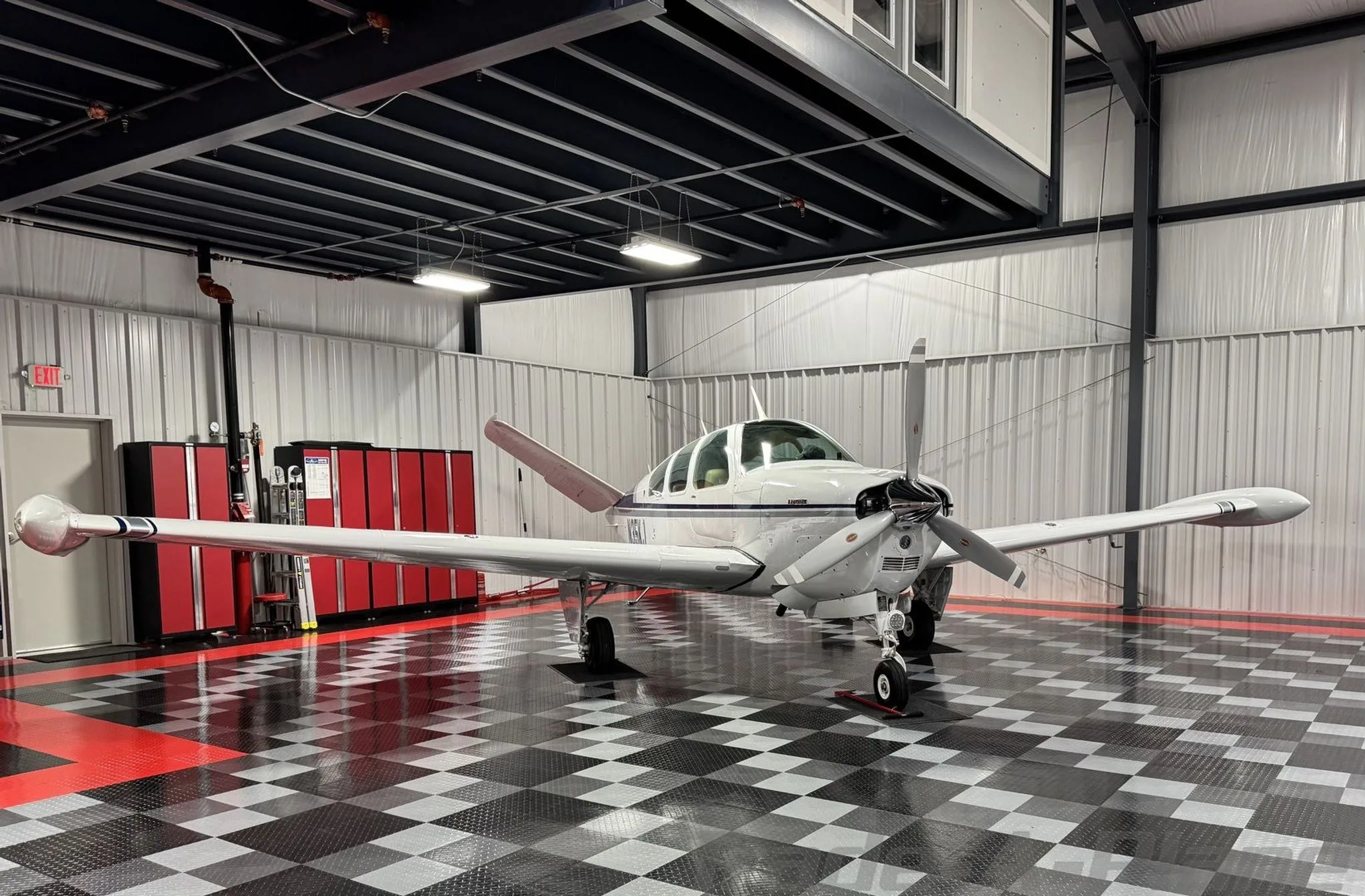 A white Beechcraft Bonanza with blue and grey stripes parked head-on in a hangar.