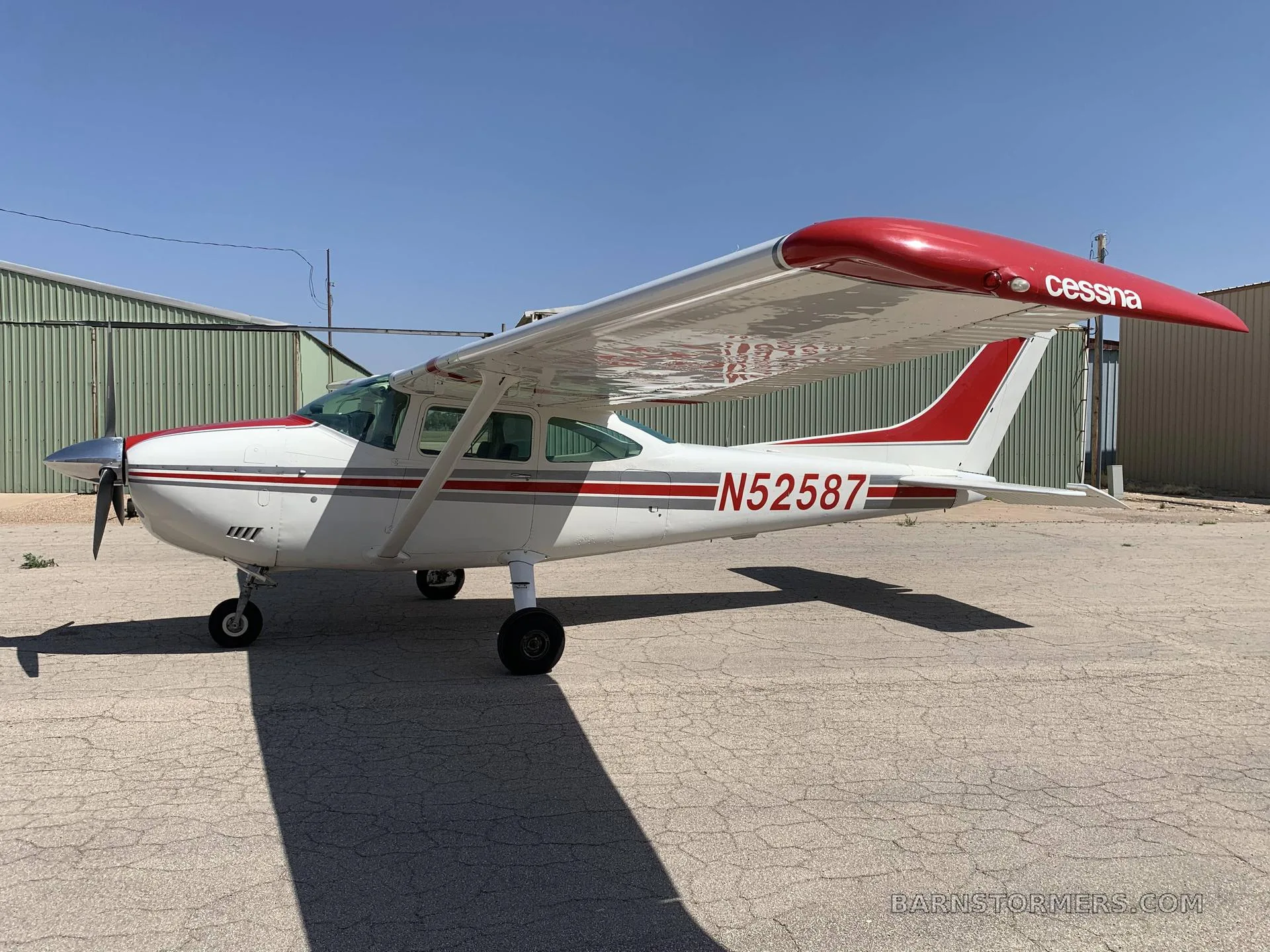 Side view of a white and red Cessna single-engine aircraft (N52587) parked on an asphalt ramp.