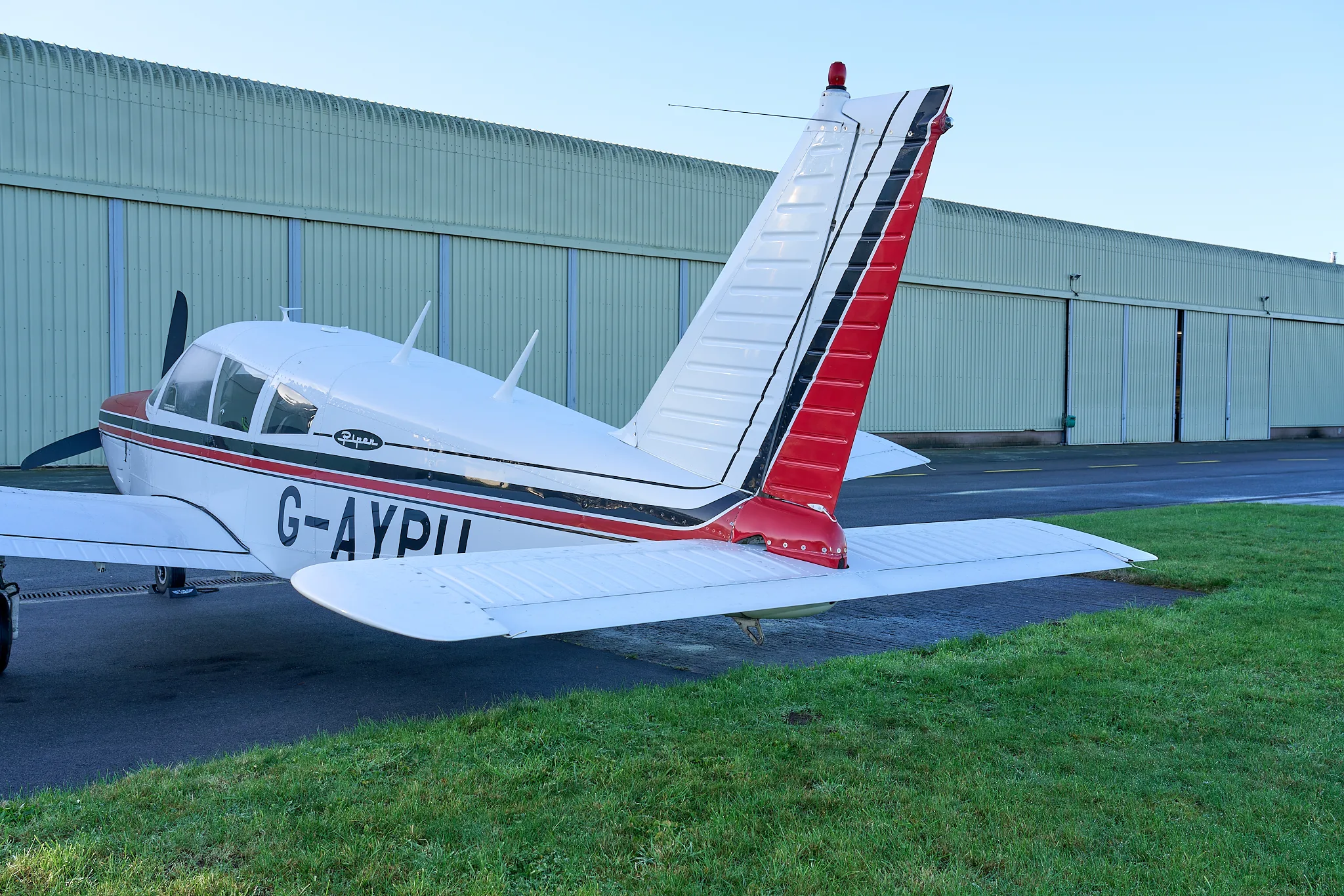 A close-up rear-side view of the white and red Piper Cherokee G-AYPU's tail section.