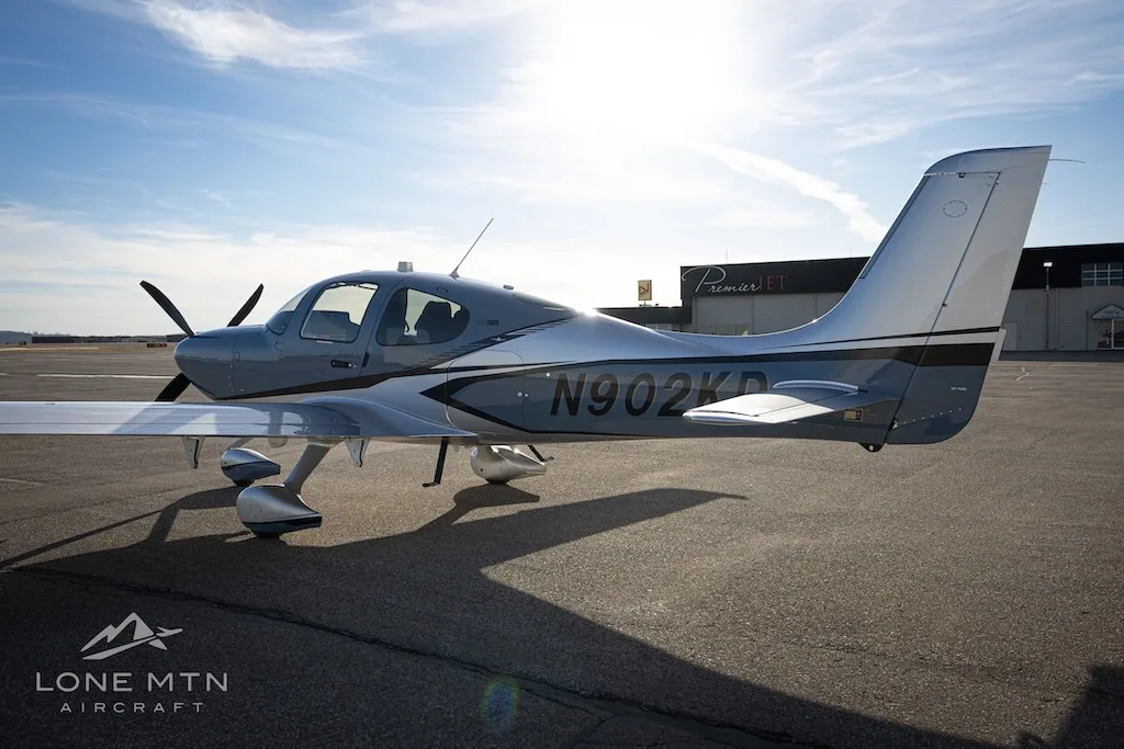 A three-quarter rear view of the Cirrus SR22T aircraft, N902KD, in blue and silver, on an airfield.