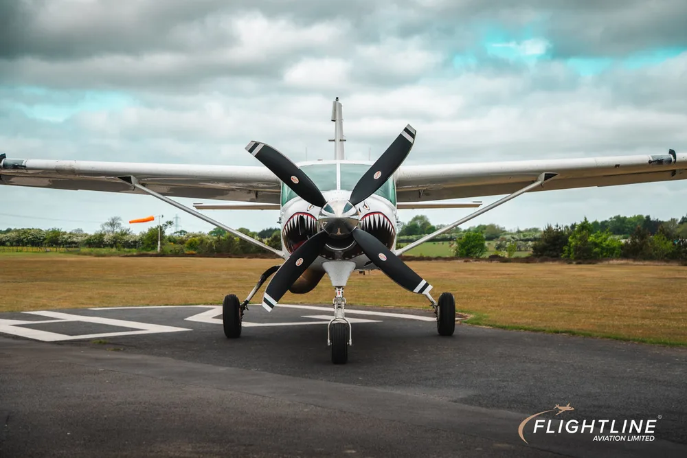 Front view of a white Cessna 208 Caravan with shark teeth nose art, parked on a runway.