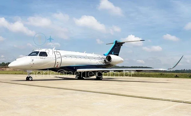 A white and blue Embraer Praetor 600 business jet parked on a tarmac under a partly cloudy sky.