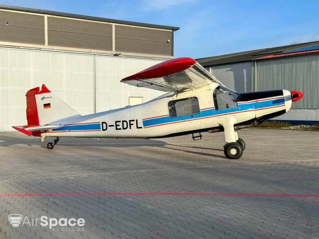 A side view of a white aircraft with blue and red stripes and a red tail, parked on a paved apron.