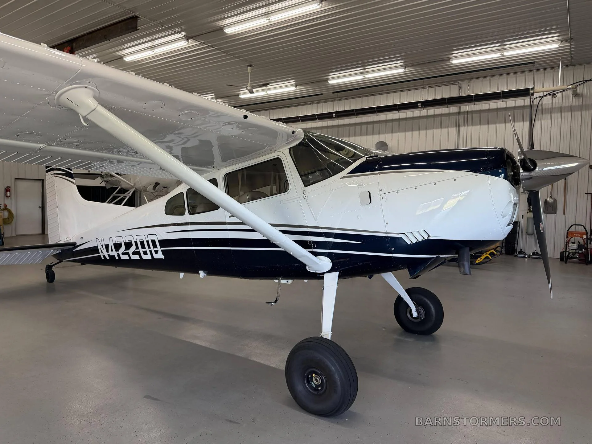 A white and blue single-engine propeller aircraft with tail number N42200 is parked inside a hangar.