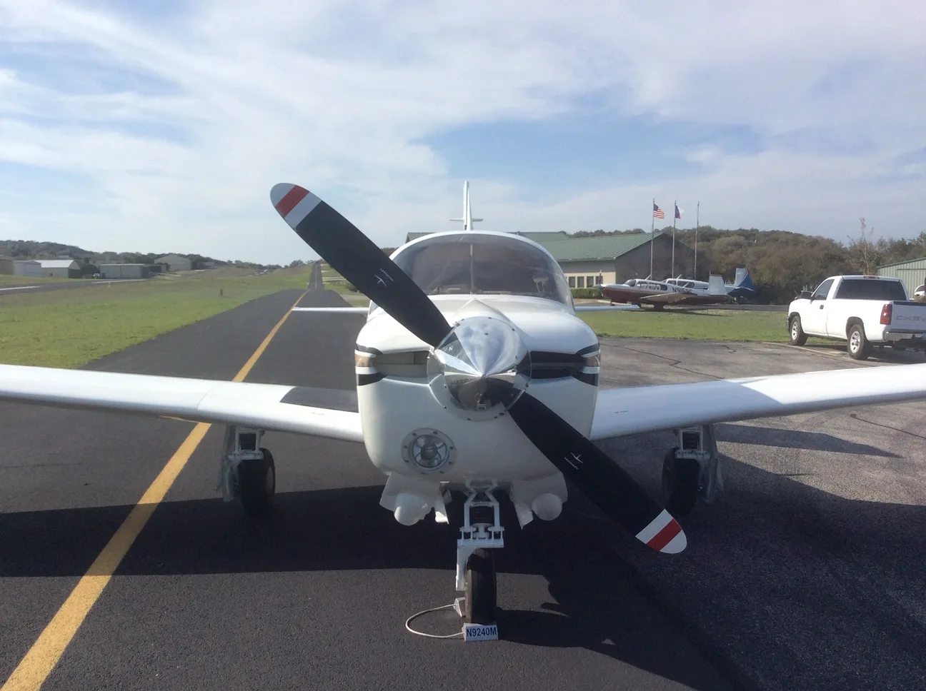 Frontal view of a white Piper PA-28-180 Cherokee with dark stripes, parked on an airfield tarmac.